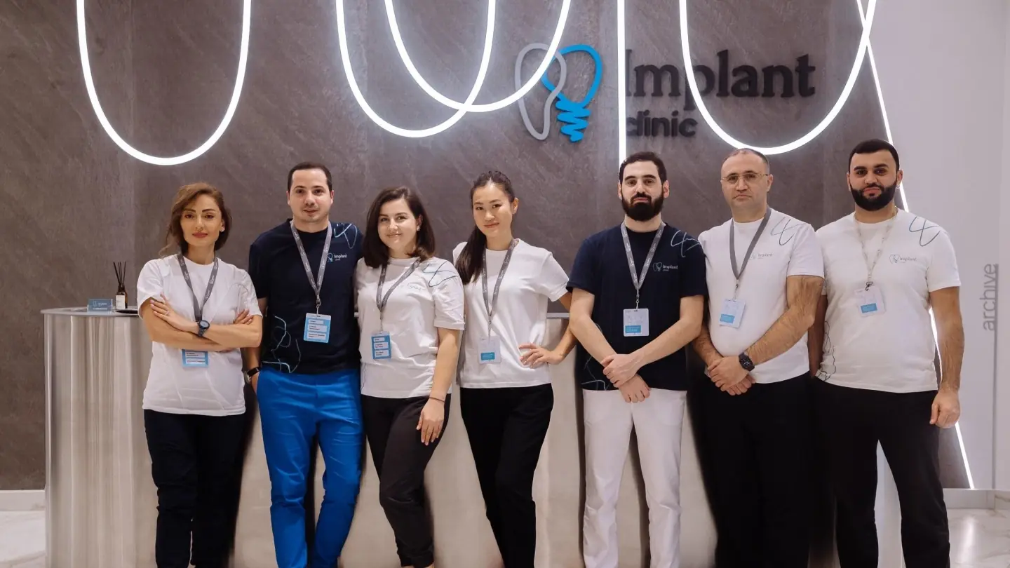 Команда клиники Implant Clinic у стойки ресепшена с фирменной вывеской